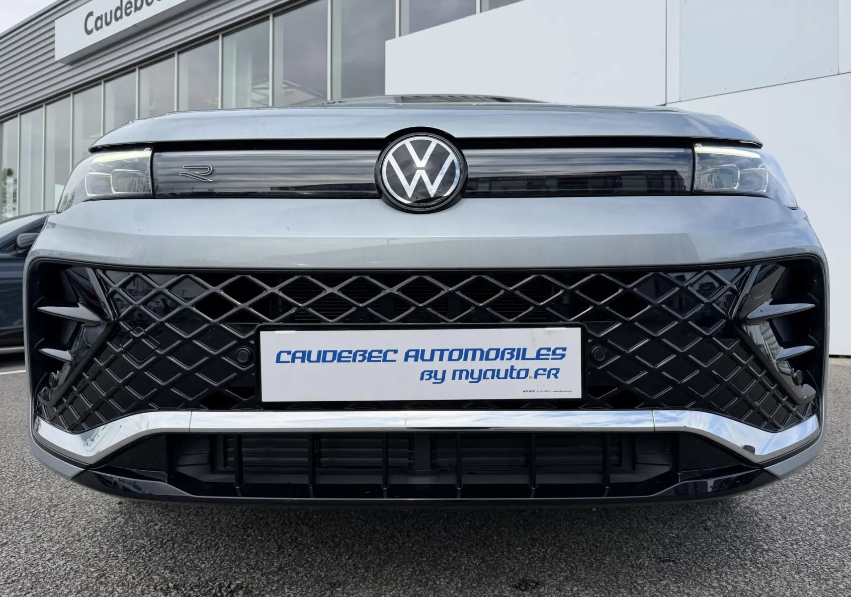 Vue frontale rapprochée du Volkswagen Tiguan gris 2025 avec calandre noire à motif losange et logo VW central lumineux.