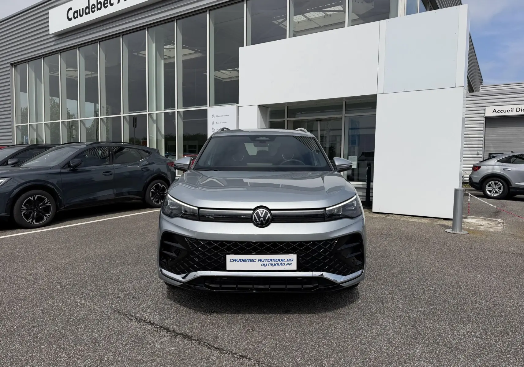 Vue avant d'un Volkswagen Tiguan gris métallisé 2025 avec calandre noire et phares LED, devant un concessionnaire.