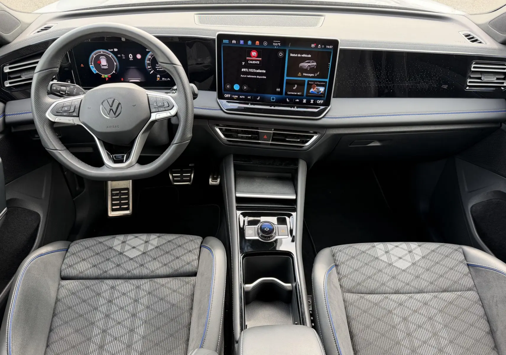 Vue intérieure avant du Volkswagen Tiguan 2025, tableau de bord digital et sièges sport gris avec surpiqûres bleues.