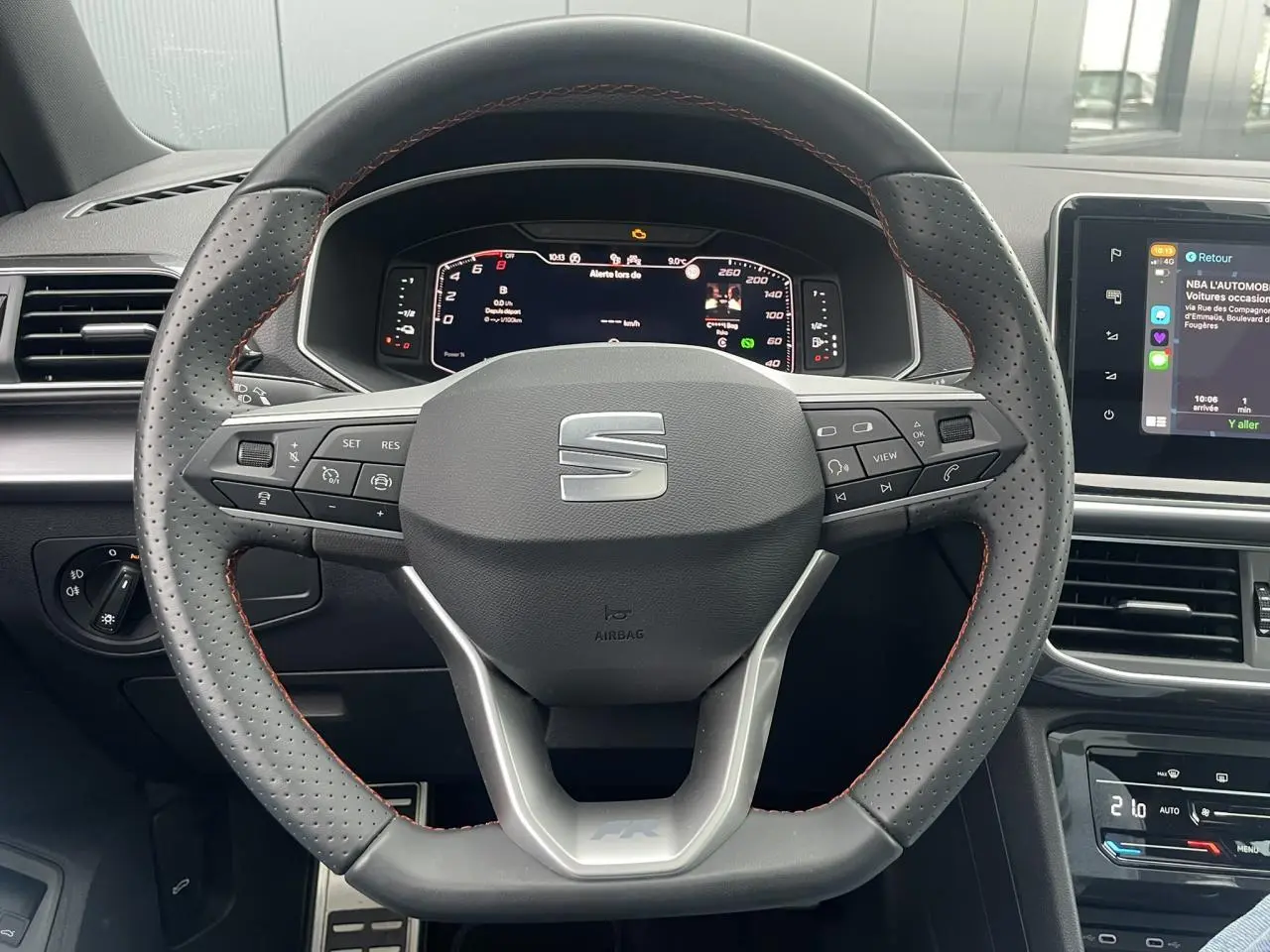 Volant sport en cuir avec surpiqûres rouges et tableau de bord numérique du SEAT Tarraco FR gris dauphin, vue de face intérieure.