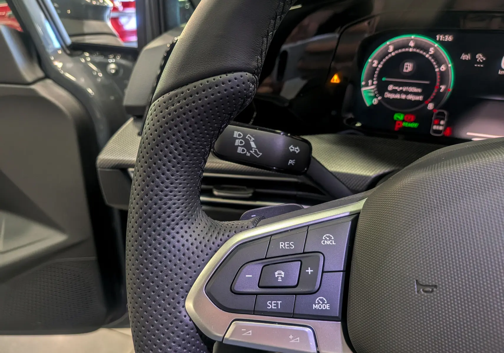 Gros plan sur le volant perforé côté gauche de la Volkswagen Golf VIII gris Urano avec commandes intégrées et tableau de bord numérique.