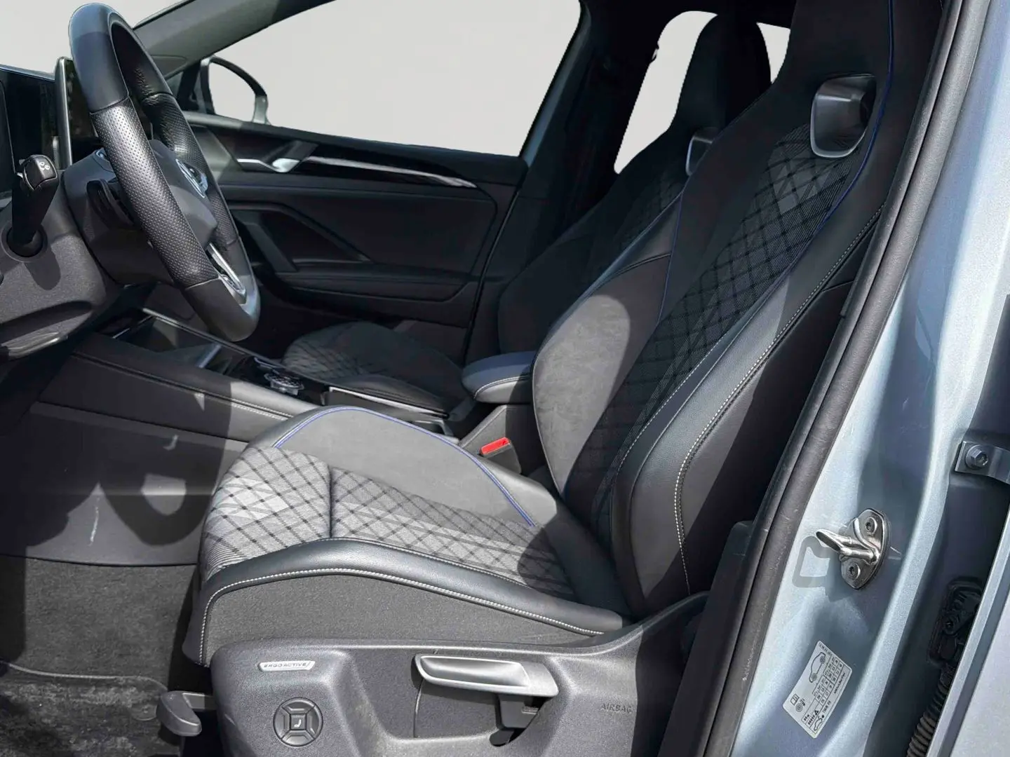 Vue intérieure côté conducteur du Volkswagen Tiguan gris 2025, sièges sport ErgoActive avec surpiqûres et volant cuir multifonction.