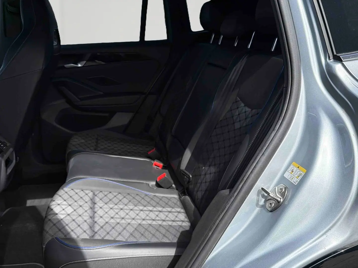 Vue intérieure côté arrière droit du Volkswagen Tiguan 2025, montrant les sièges arrière en cuir noir avec surpiqûres bleues.