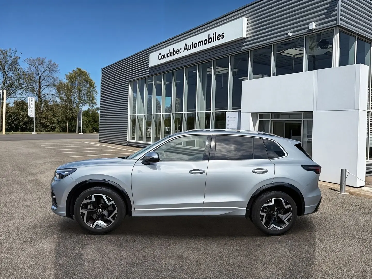 Vue de profil côté gauche d'un Volkswagen Tiguan gris métallisé avec jantes alliage noires devant un bâtiment de concession.