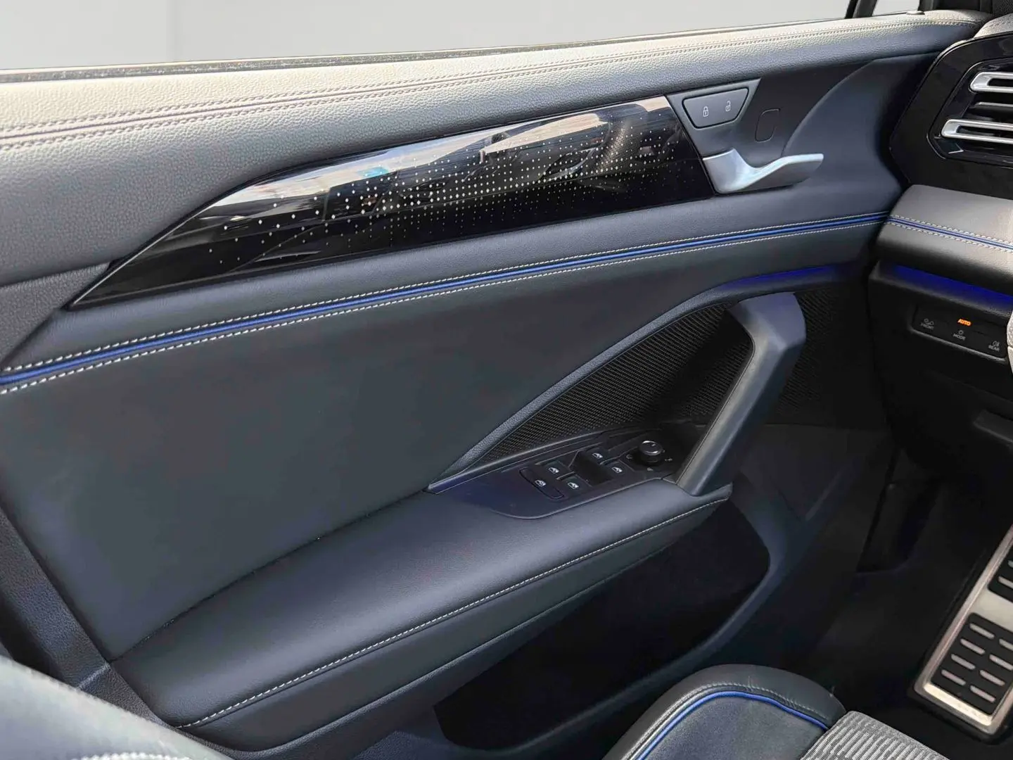 Vue intérieure côté gauche de la porte avant du Volkswagen Tiguan 2025 avec surpiqûres bleues et commandes électriques.