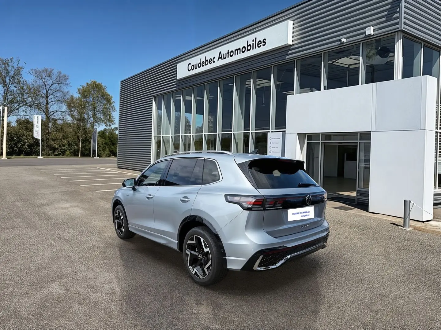 Vue 3/4 arrière du Volkswagen Tiguan gris métallisé 2025 avec jantes alliage noires devant un concessionnaire.