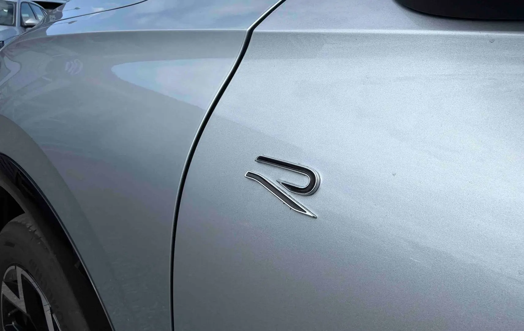 Détail du logo R sur l'aile avant gauche d'un Volkswagen Tiguan gris métallisé, avec jante noire visible.