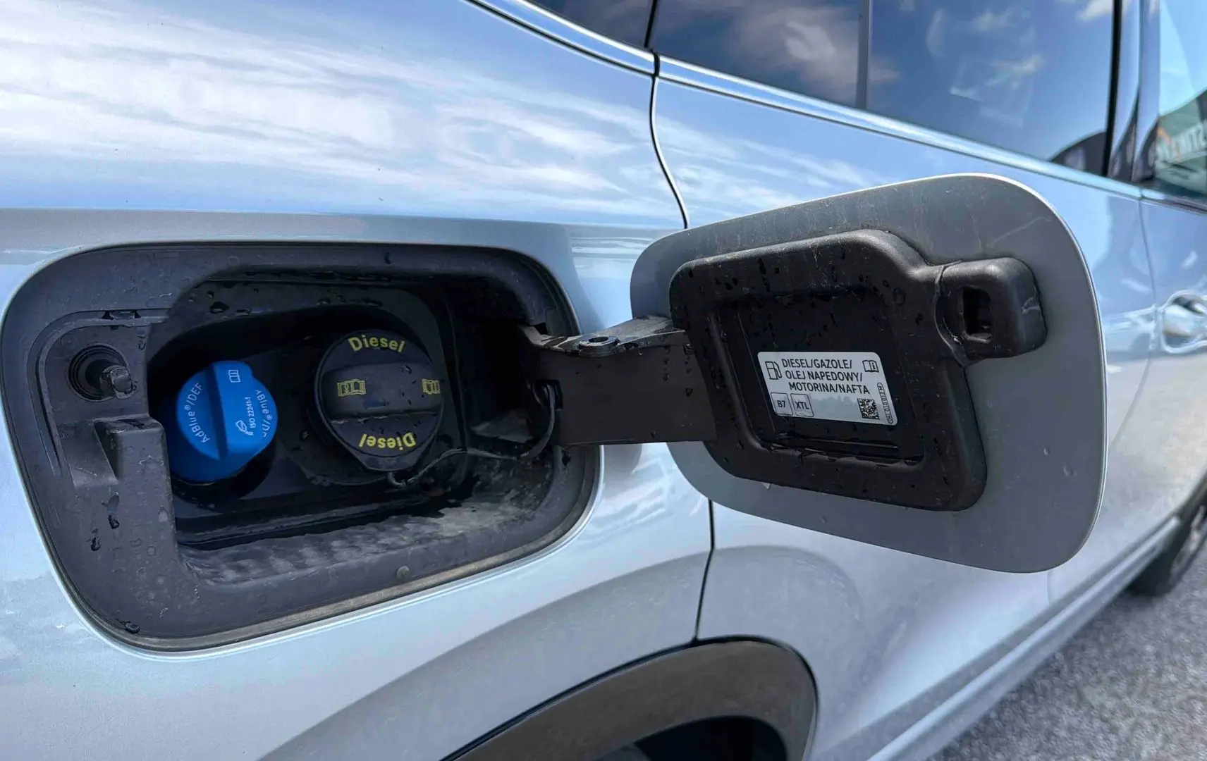 Gros plan sur la trappe à carburant ouverte côté gauche d’un Volkswagen Tiguan gris 2025 avec bouchon diesel visible.