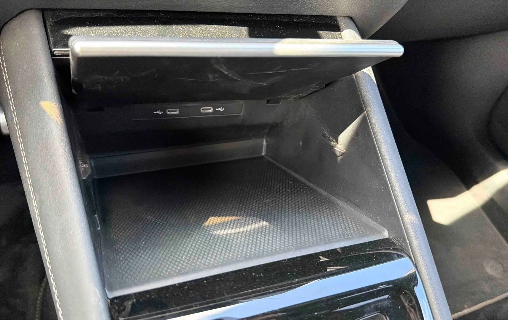 Rangement central ouvert avec deux ports USB-C visibles, intérieur noir mat et garniture cuir gris clair.