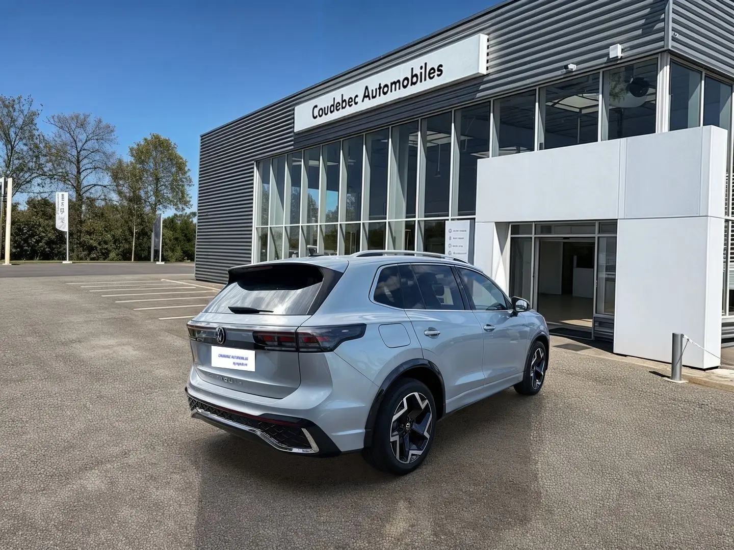 Volkswagen Tiguan gris en 3/4 arrière droit, avec jantes noires brillantes, stationné devant un concessionnaire.