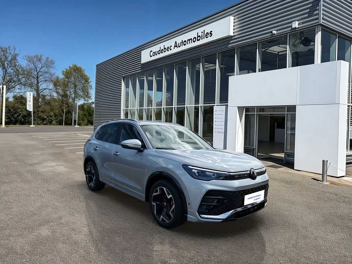 Volkswagen Tiguan gris en 3/4 avant droit, avec jantes noires brillantes et calandre moderne, devant un concessionnaire.