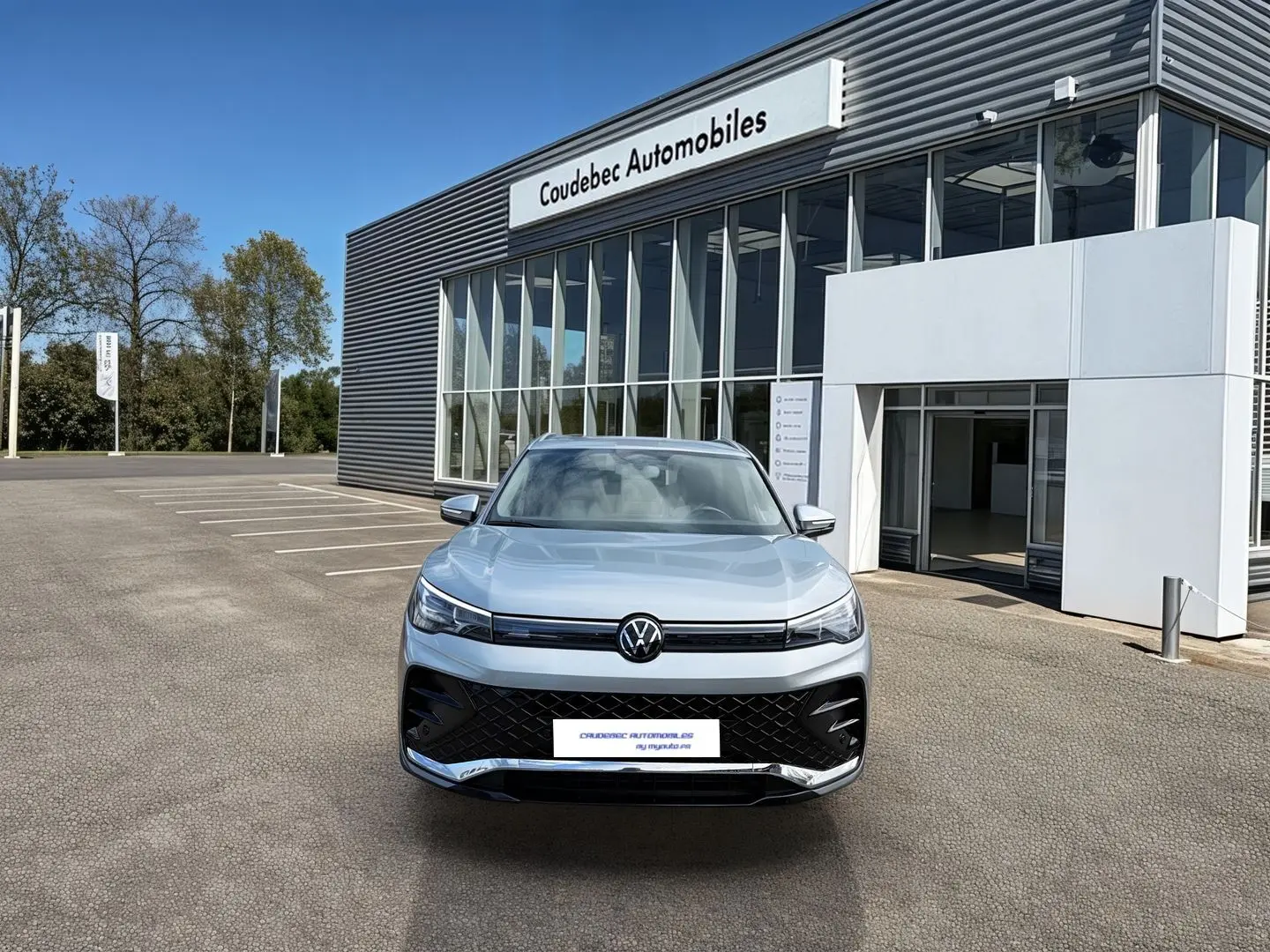 Vue avant d'un Volkswagen Tiguan gris 2025 garé devant un bâtiment moderne de concession automobile.