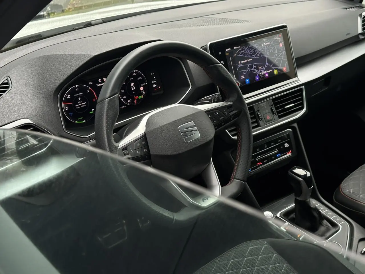 Vue intérieure du poste de conduite du SEAT Tarraco blanc, volant cuir multifonction et écran tactile de navigation visible.