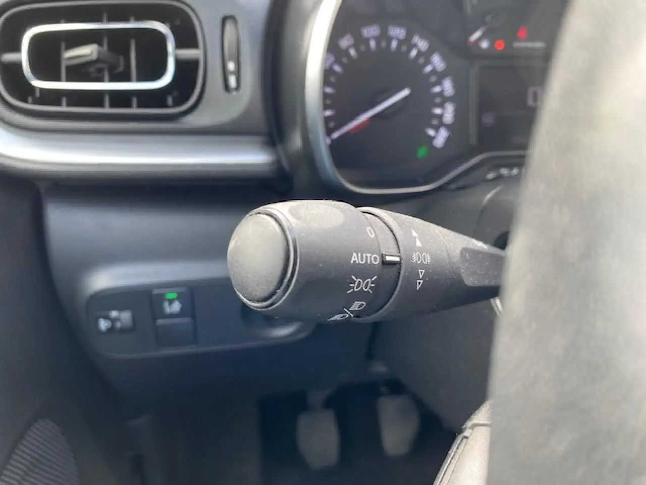 Gros plan sur la commande d'éclairage à gauche du volant dans l'habitacle d'une Citroën C3 gris clair de 2017.
