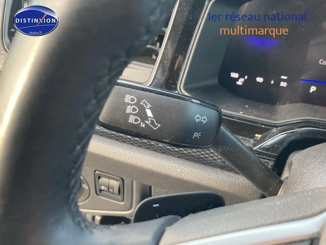 Gros plan sur le commodo gauche et le volant cuir de la Volkswagen Polo gris cendre, tableau de bord digital en arrière-plan.