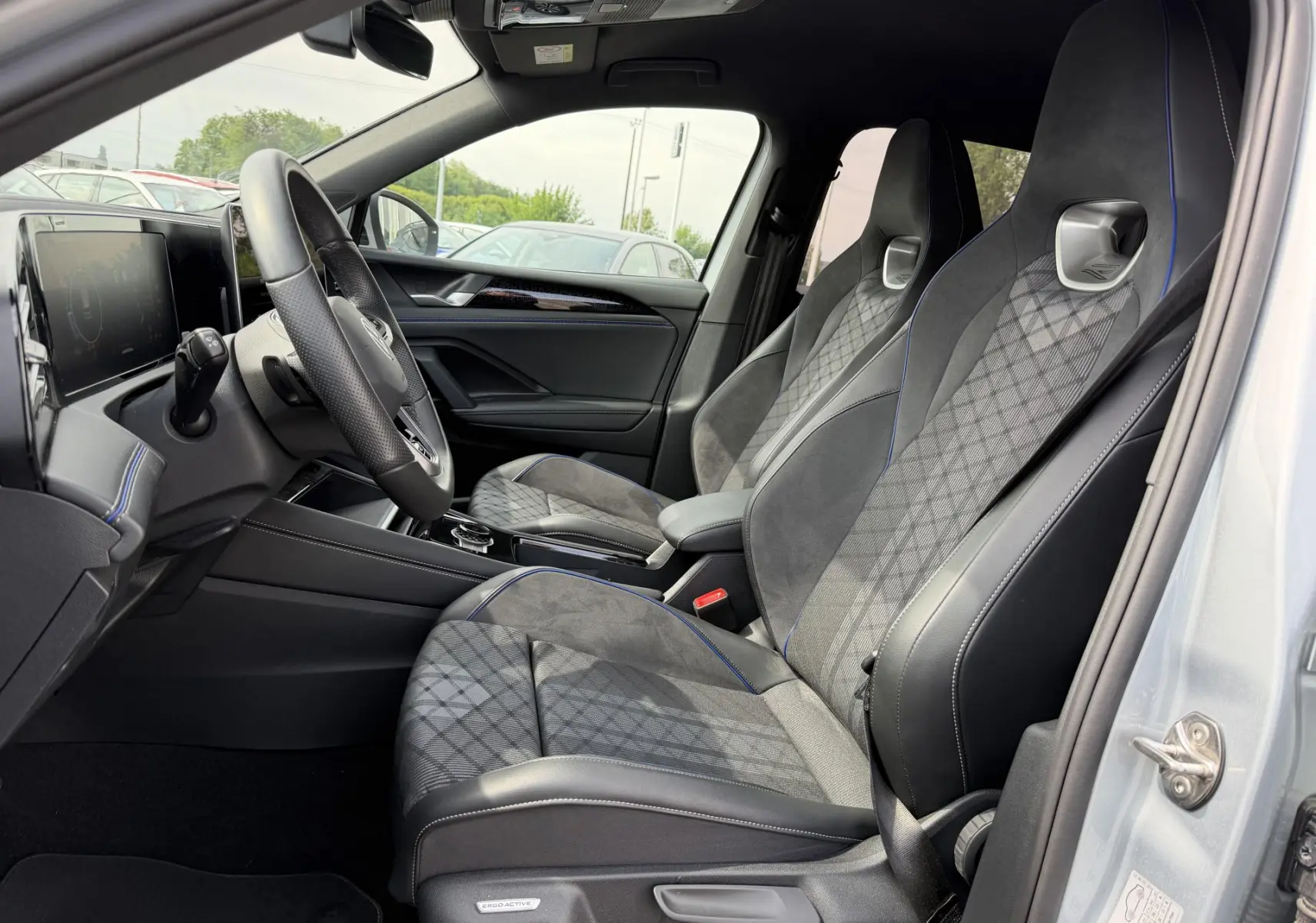 Vue intérieure côté conducteur du Volkswagen Tiguan 2025, sièges sport gris avec surpiqûres bleues et volant multifonction cuir.
