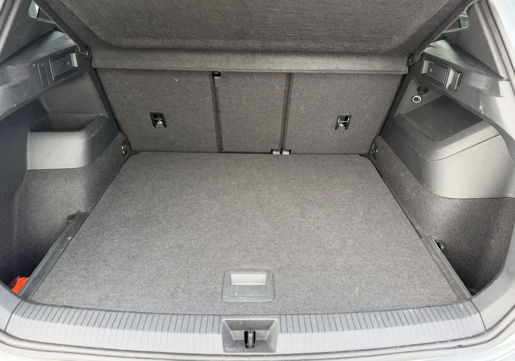 Coffre ouvert du Volkswagen Tiguan gris, vue arrière montrant l'espace de chargement et les rangements latéraux.
