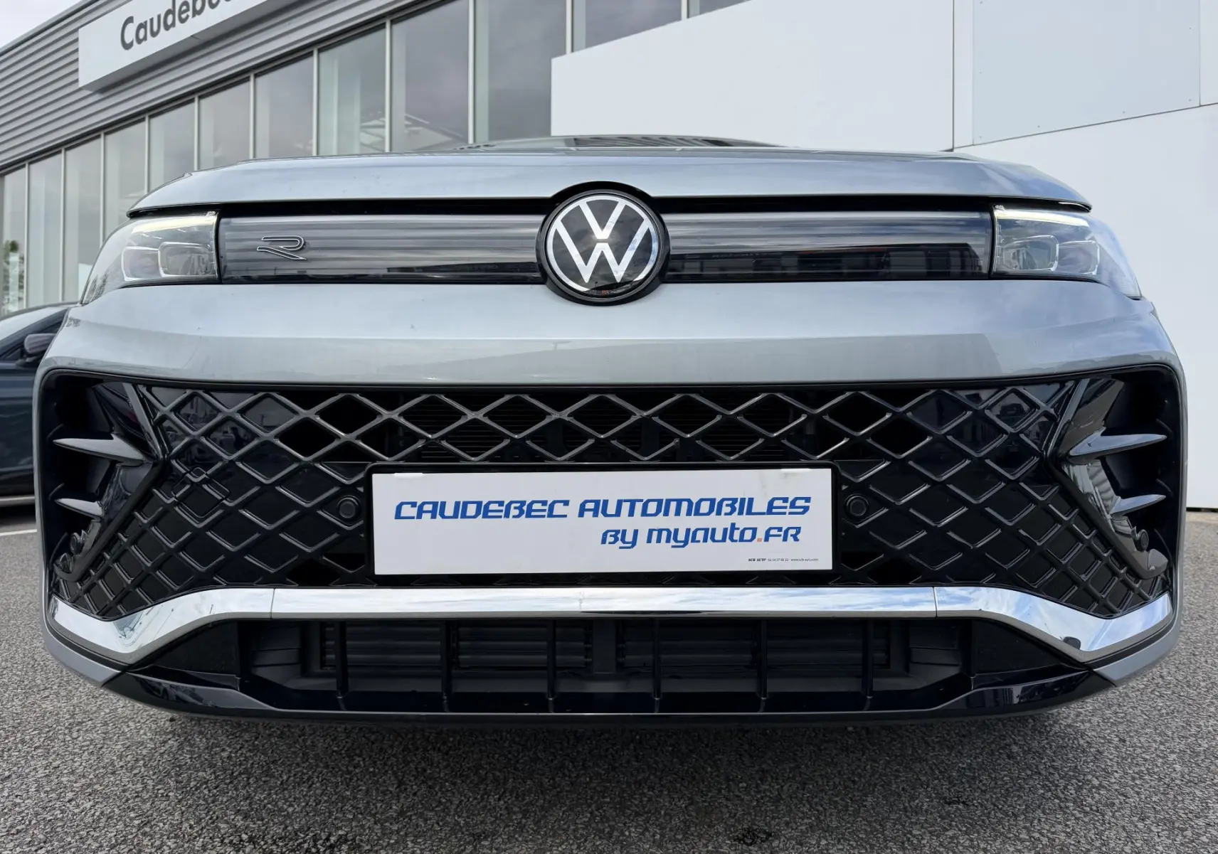 Vue frontale du Volkswagen Tiguan gris avec calandre noire à motif losange et logo VW central lumineux.