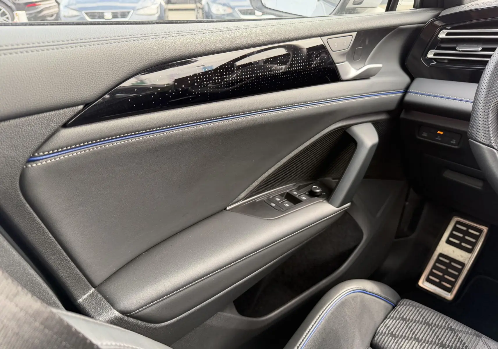 Vue intérieure côté gauche du Volkswagen Tiguan 2025, porte en cuir noir avec surpiqûres bleues et commandes électriques.