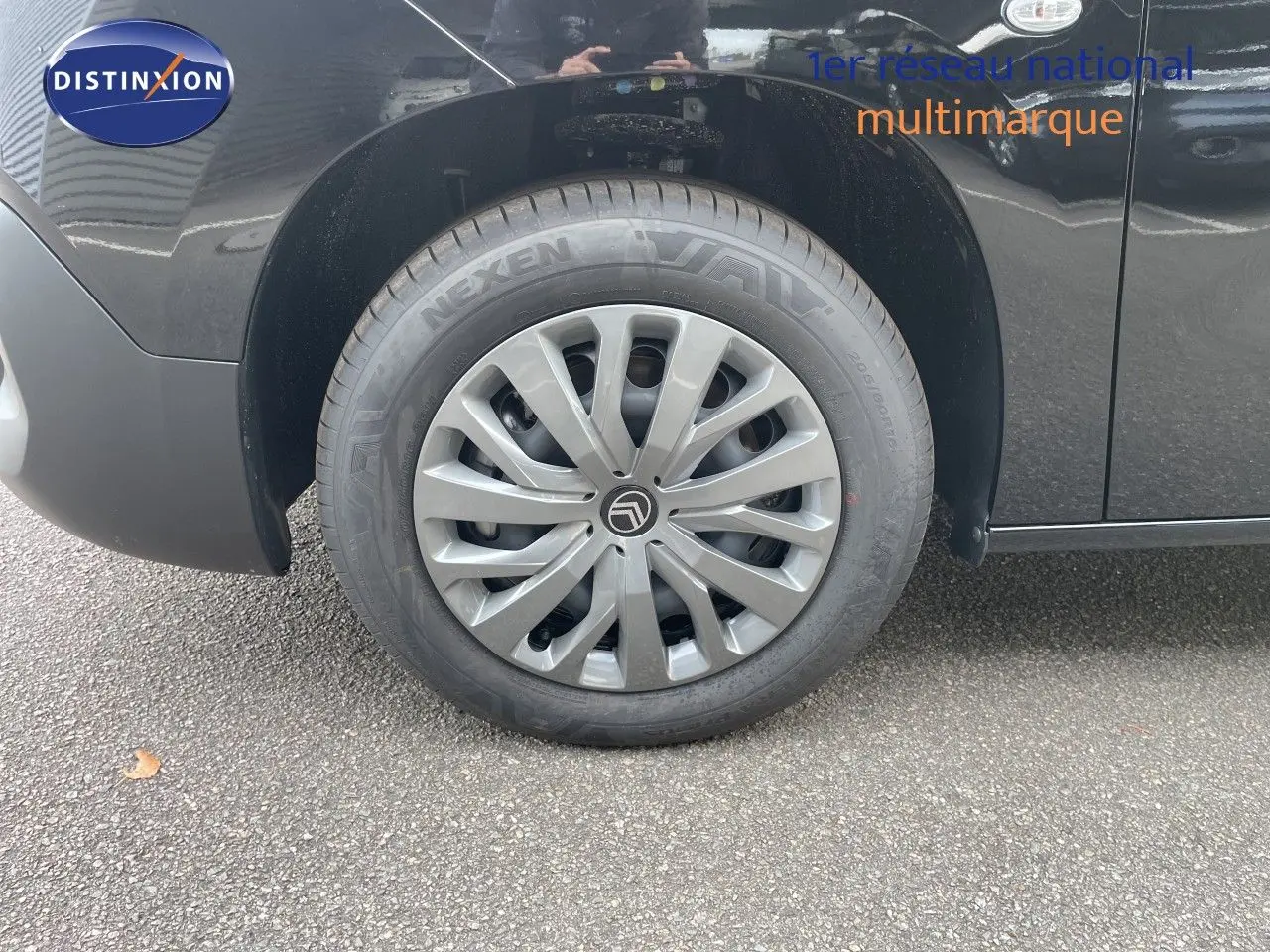 Gros plan sur la roue avant gauche d'un Citroën Berlingo noir Perla Nera métal avec jante argentée et logo Citroën.