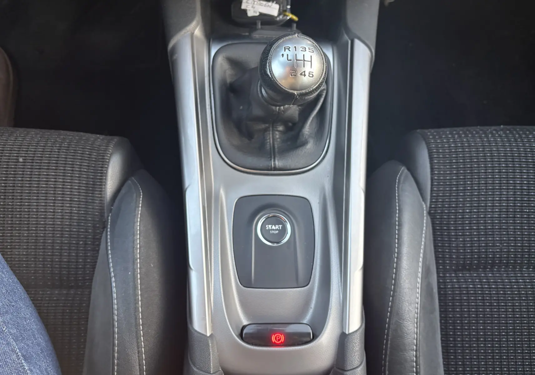 Vue plongeante sur la console centrale d'une Citroën C4 II 2.0 HDI 150 HYB 2015 avec levier de vitesse manuel et bouton start/stop.