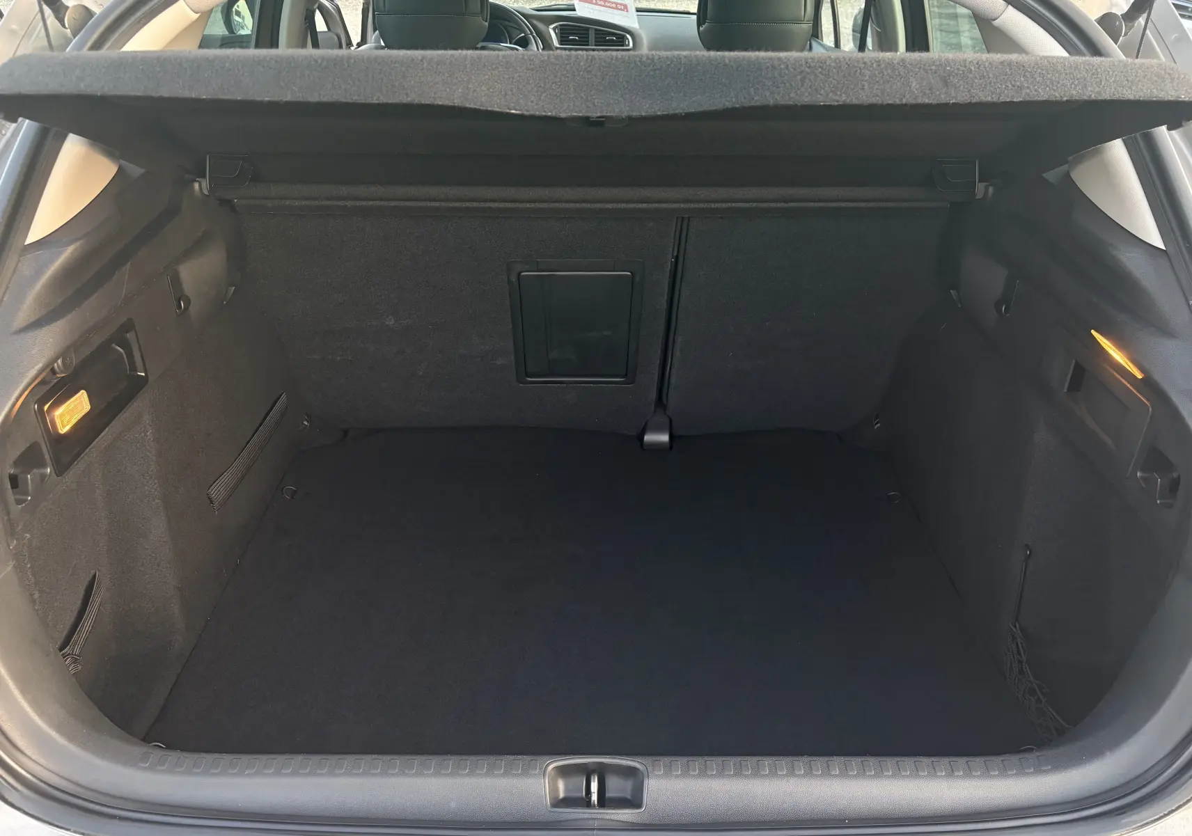 Coffre ouvert d'une Citroën C4 II 2.0 HDI 150 HYB 2015, vue intérieure arrière, tapis noir et éclairage latéral allumé.