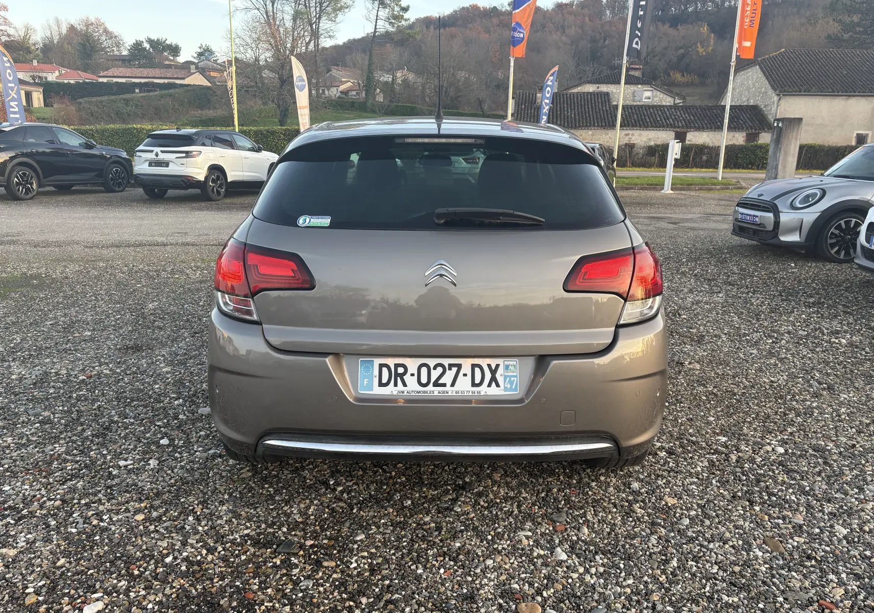 Vue arrière d'une Citroën C4 II gris métallisé avec plaque française, stationnée sur un sol gravillonné en extérieur.