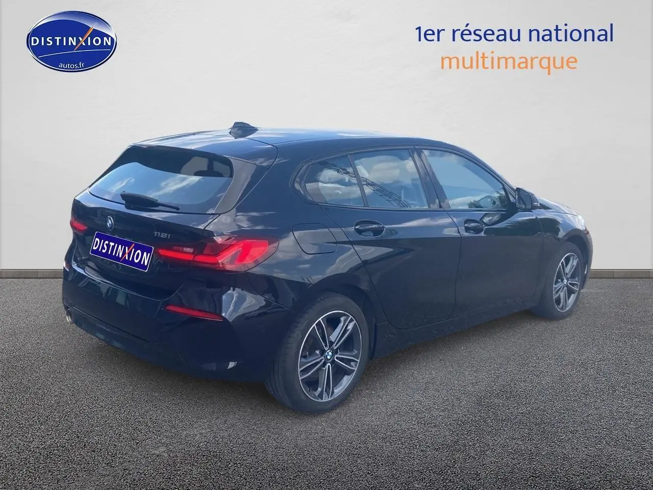 BMW Série 1 noire vue 3/4 arrière droit, avec jantes alliage et feux arrière LED allumés.