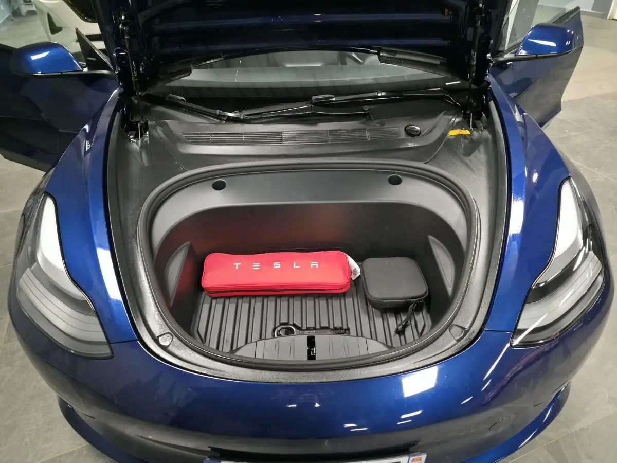 Vue plongeante sur le coffre avant ouvert d'une Tesla Model 3 RWD bleu foncé avec kit de recharge rouge visible.