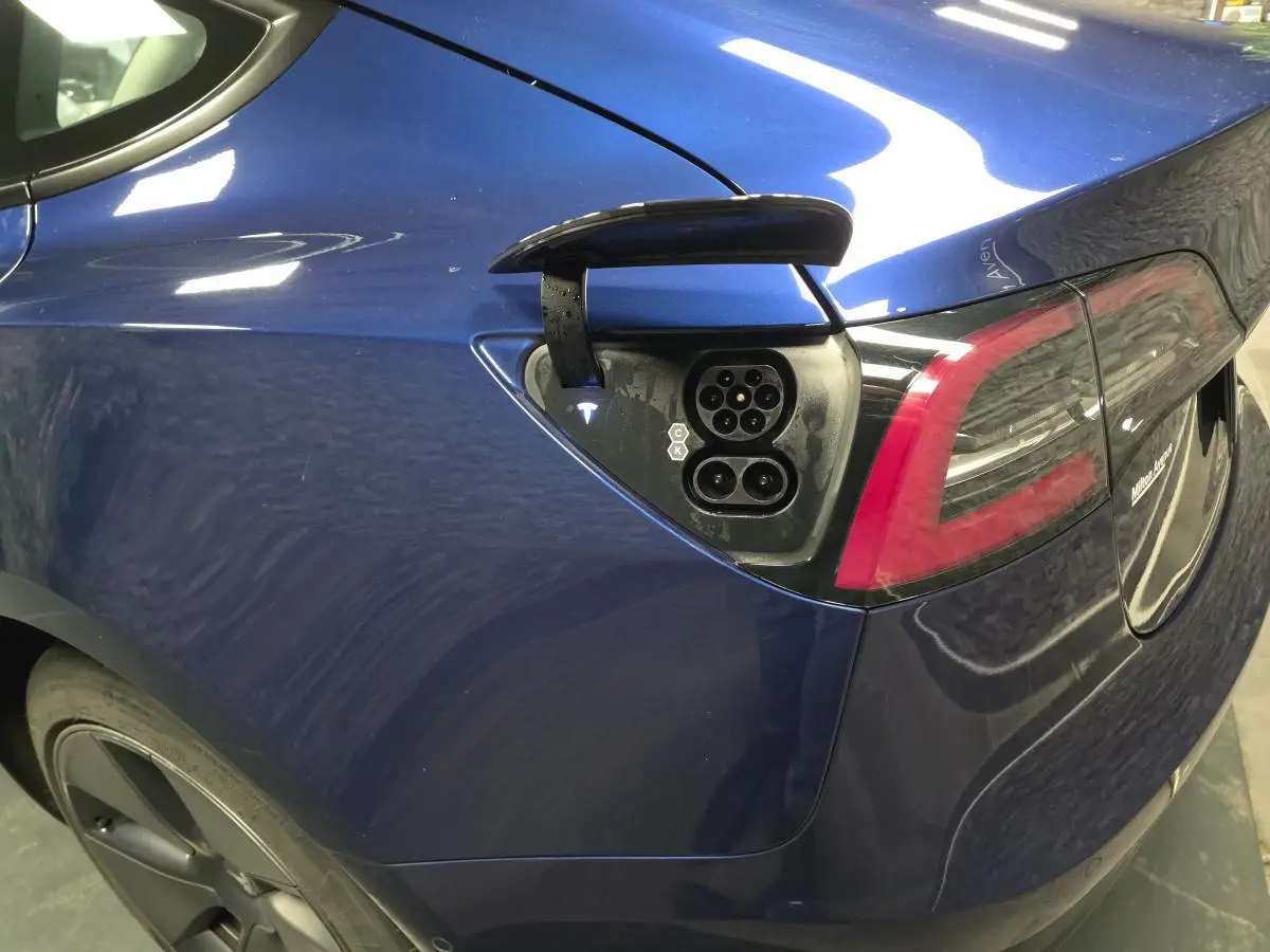 Prise de recharge ouverte sur l'aile arrière gauche d'une Tesla Model 3 RWD bleu foncé, avec feu arrière visible.