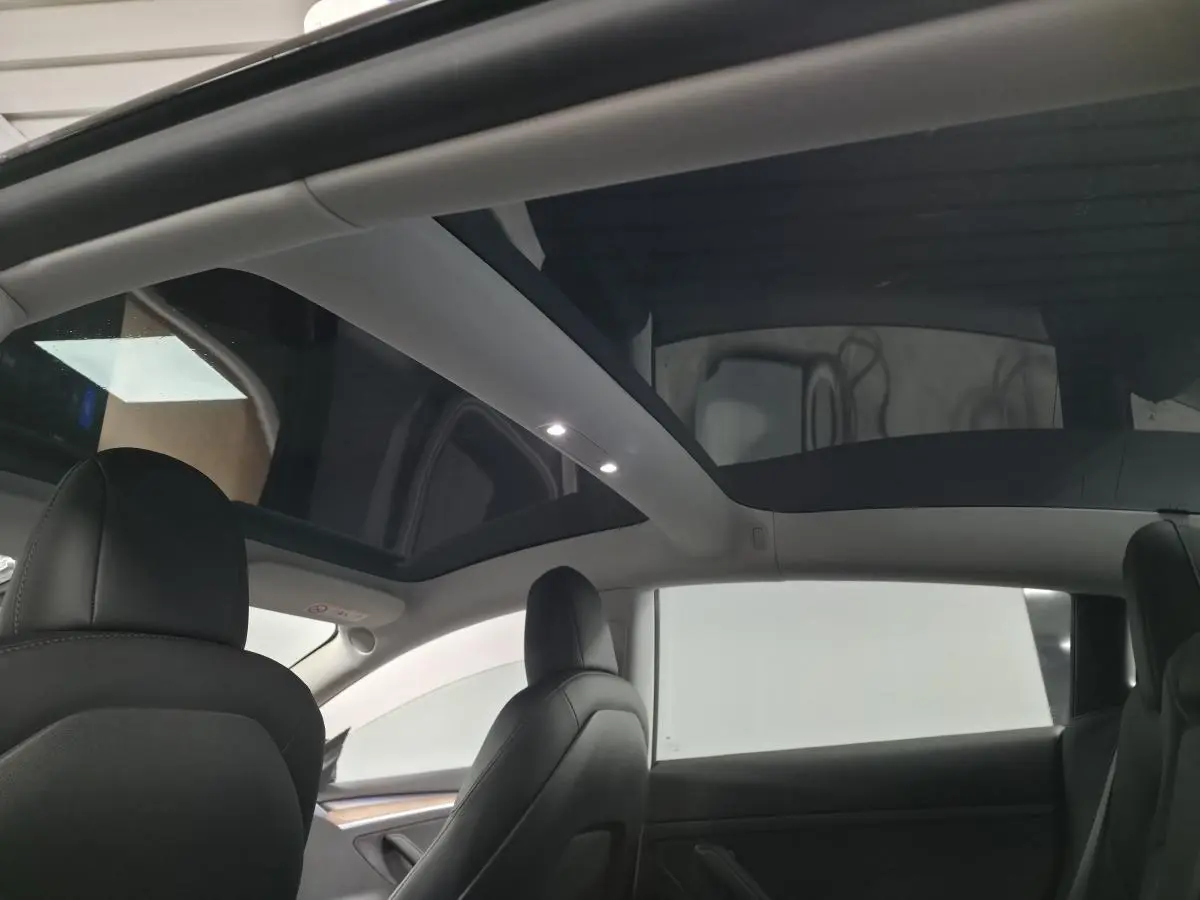 Vue intérieure arrière montrant le toit panoramique en verre et les sièges noirs d'une Tesla Model 3 RWD 2021.