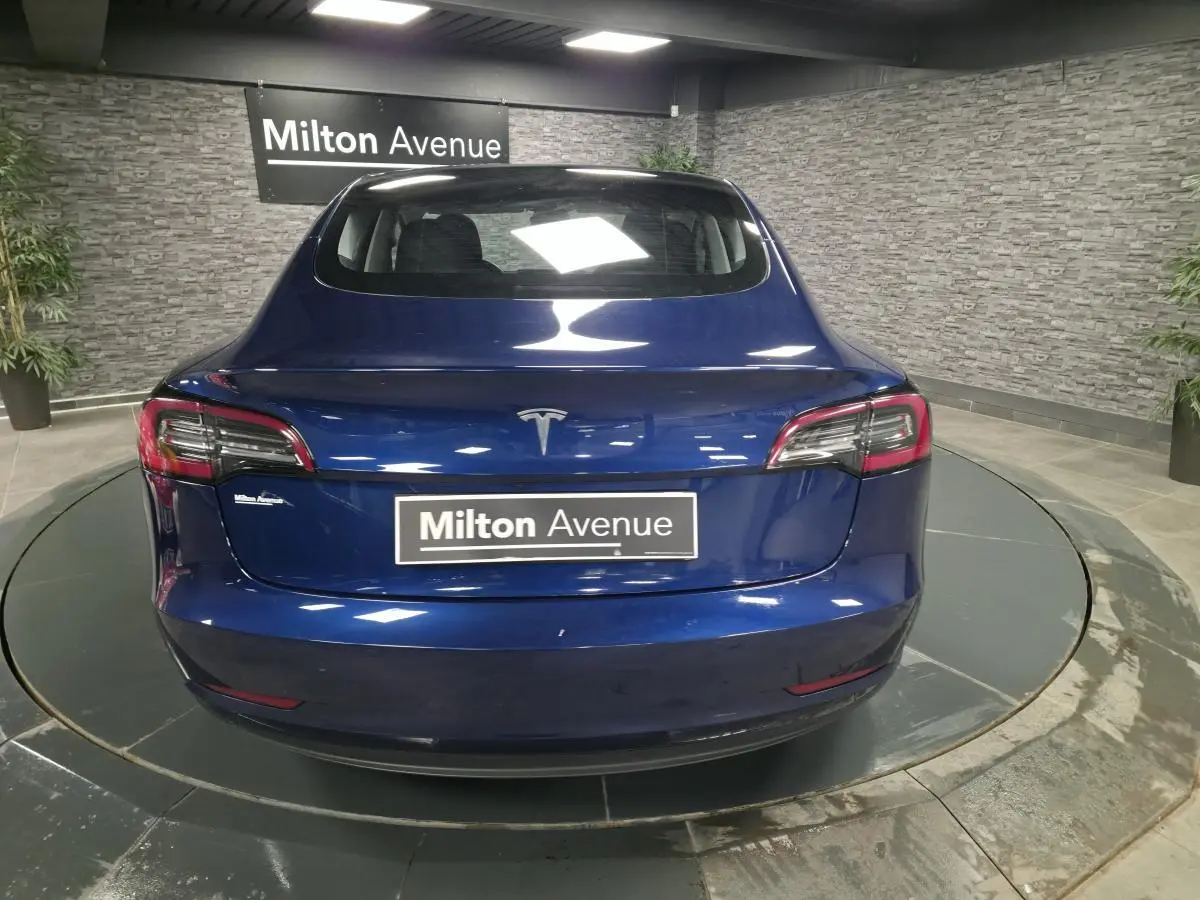 Vue arrière d'une Tesla Model 3 RWD bleu foncé avec feux LED et logo Tesla visible en intérieur showroom.