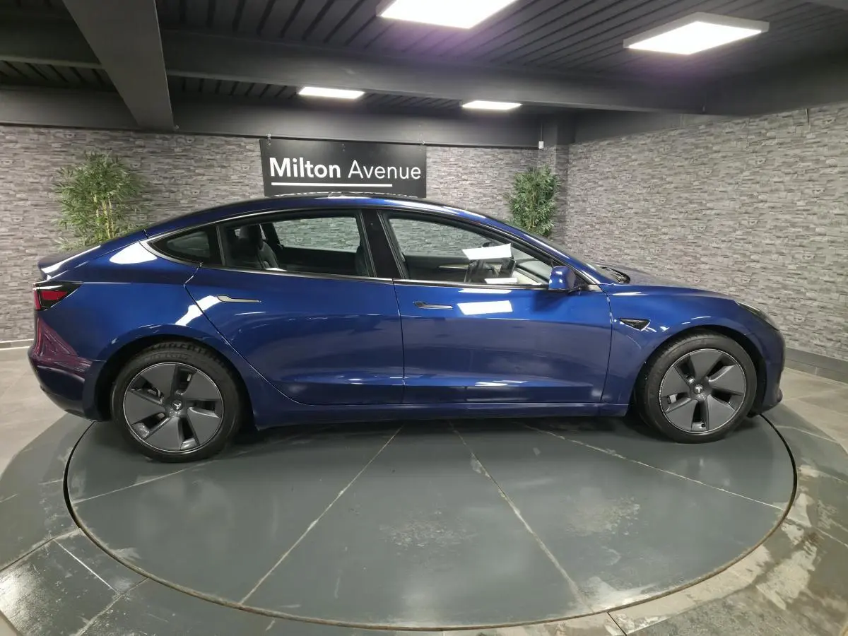 Vue latérale droite d'une Tesla Model 3 RWD 2021 bleu foncé avec jantes 18 pouces et poignées affleurantes.