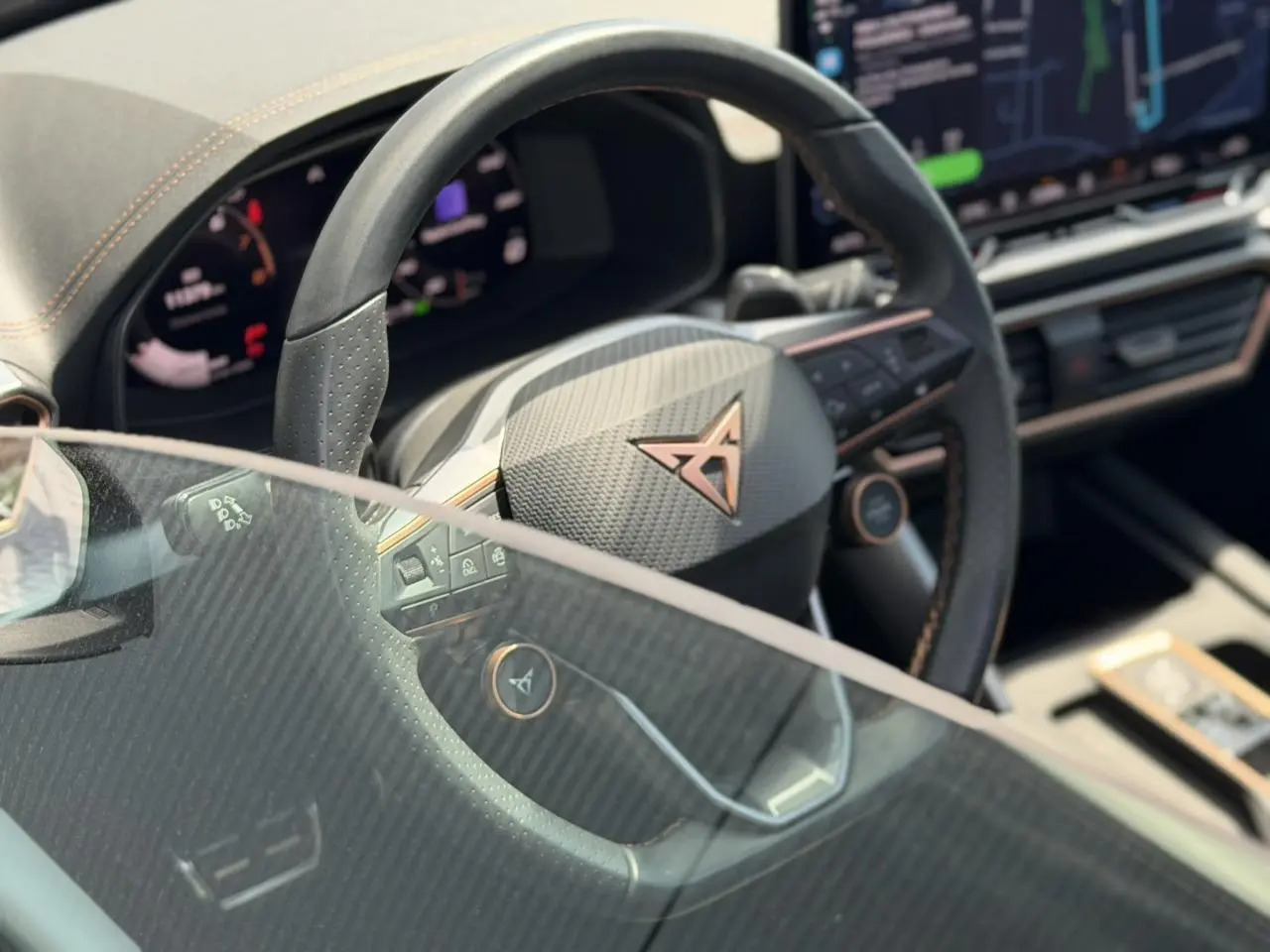 Gros plan sur le volant noir perforé avec logo CUPRA cuivré, tableau de bord numérique et écran tactile intérieur.