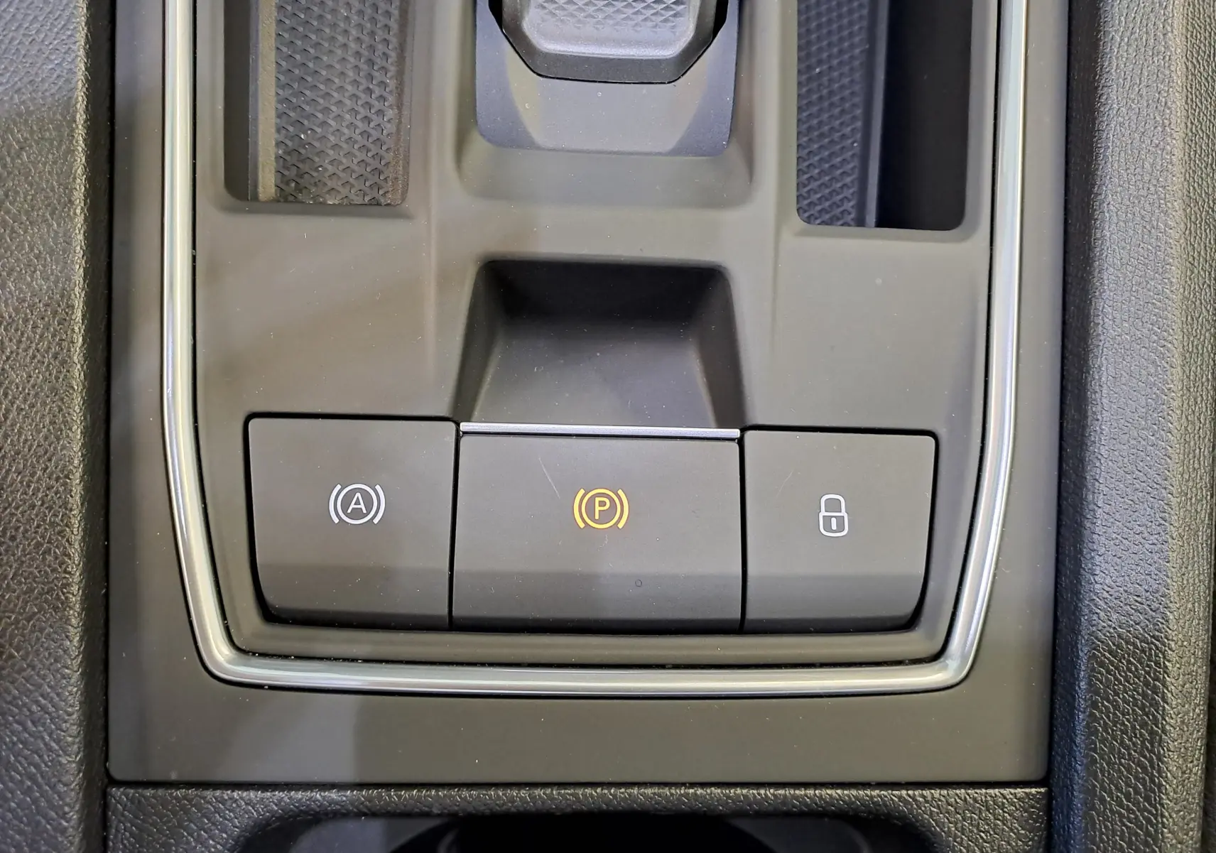 Gros plan sur la console centrale du SEAT LEON 1.5 eTSI Hybrid 2024 noir minuit, boutons de frein à main et verrouillage visibles.