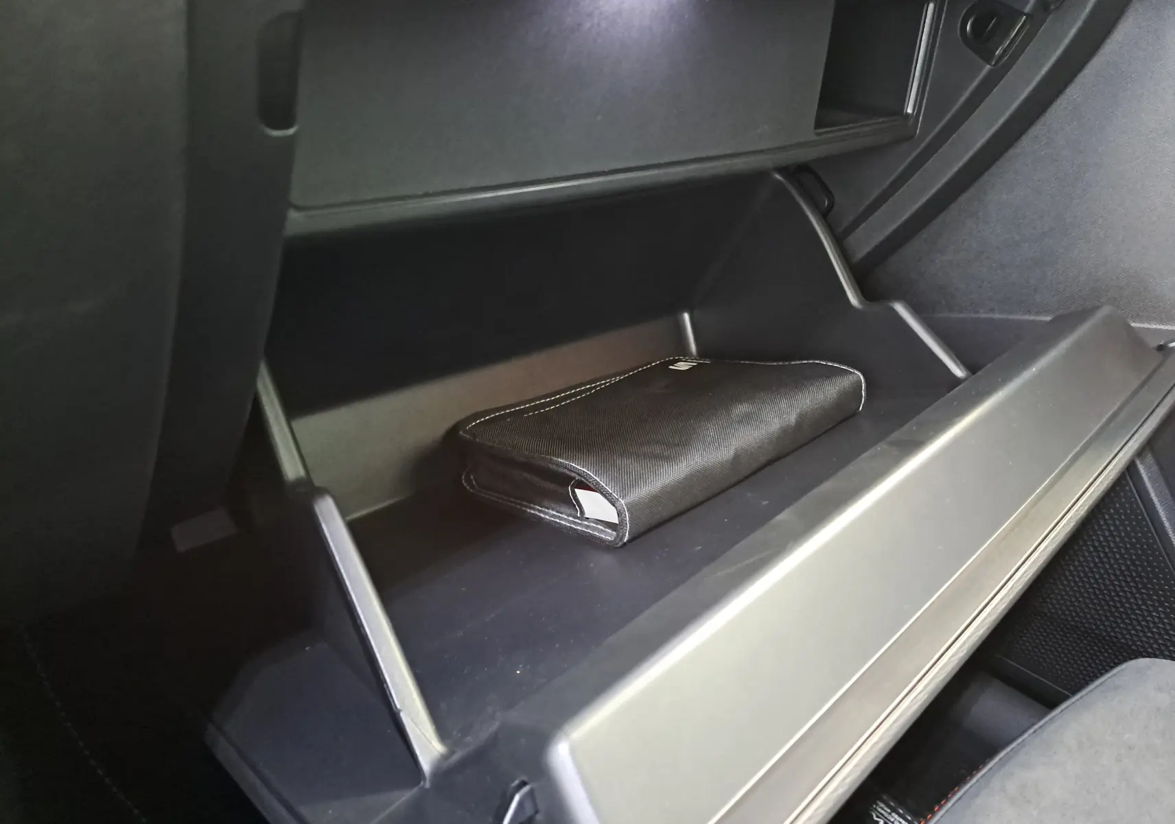 Gros plan sur la boîte à gants ouverte du SEAT LEON 1.5 eTSI Hybrid 2024, avec pochette noire à l'intérieur.