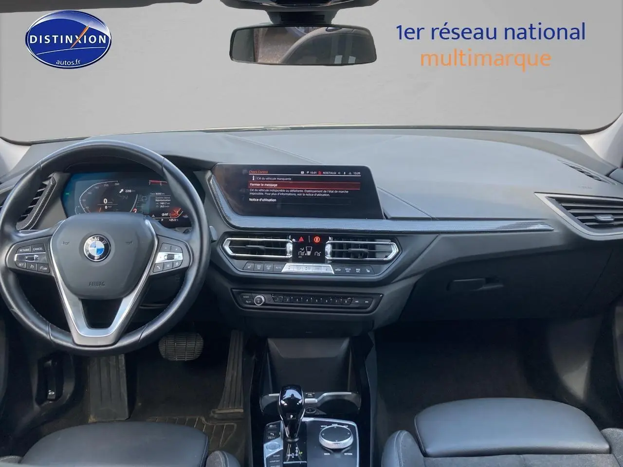 Intérieur BMW Série 1 118i 2023 vu de face, tableau de bord gris foncé avec écran central et volant multifonction.