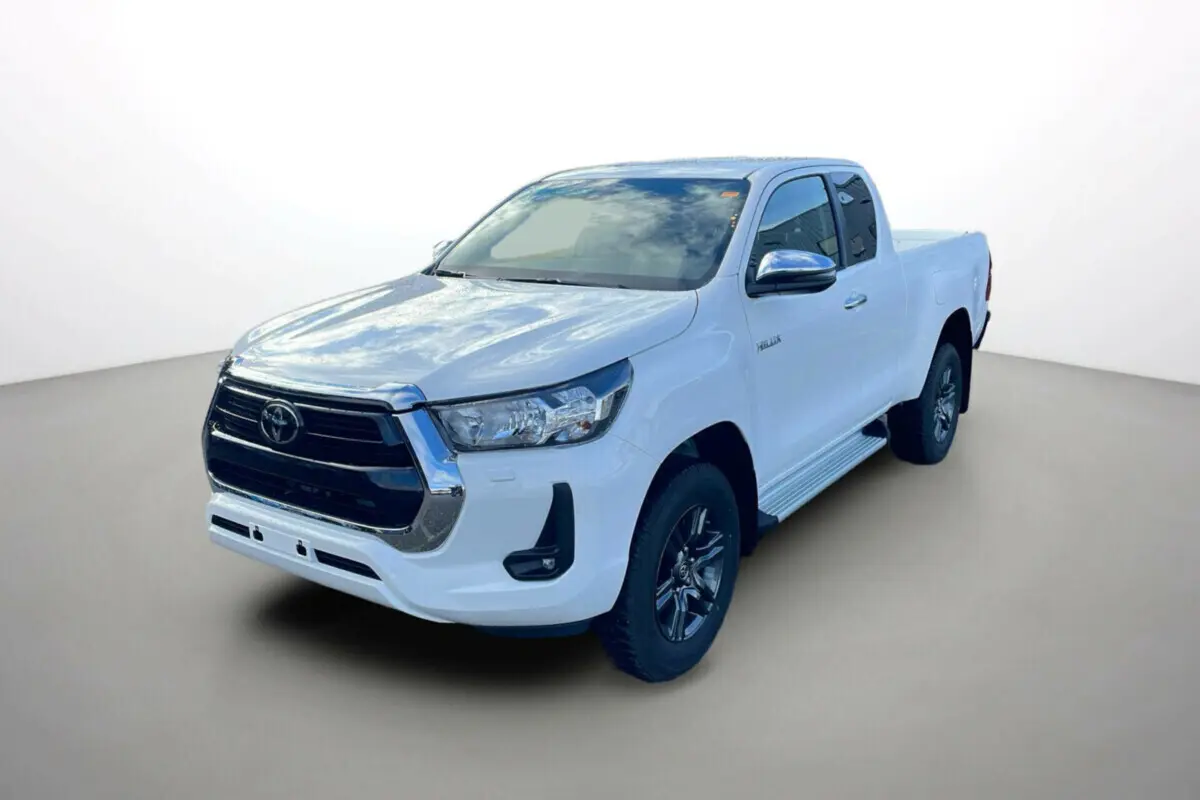 Toyota Hilux 4x4 blanc pur en 3/4 avant droit, avec calandre noire et jantes foncées distinctives.