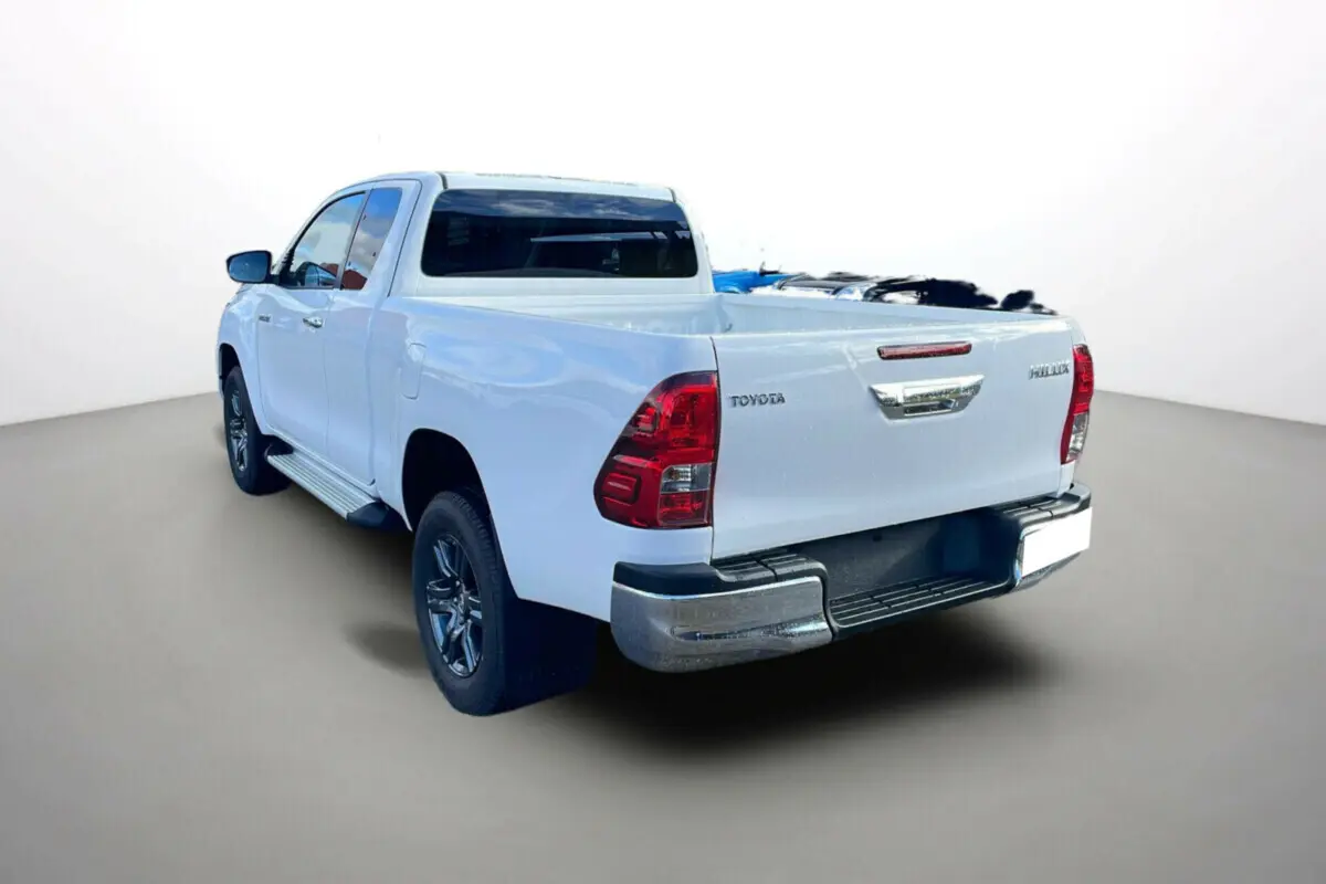 Toyota Hilux 4x4 blanc pur vu en 3/4 arrière droit, avec benne ouverte et feux arrière rouges distinctifs.