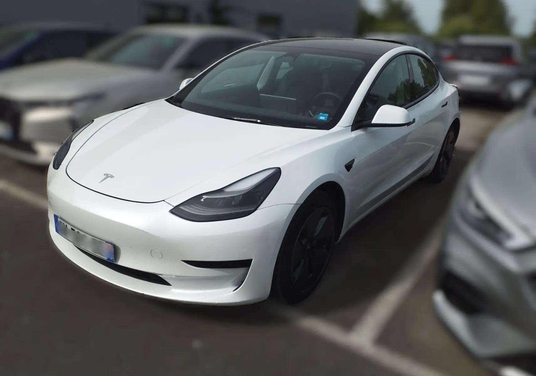 Tesla Model 3 blanc en 3/4 avant droit dans un showroom avec jantes noires et éclairage intérieur.