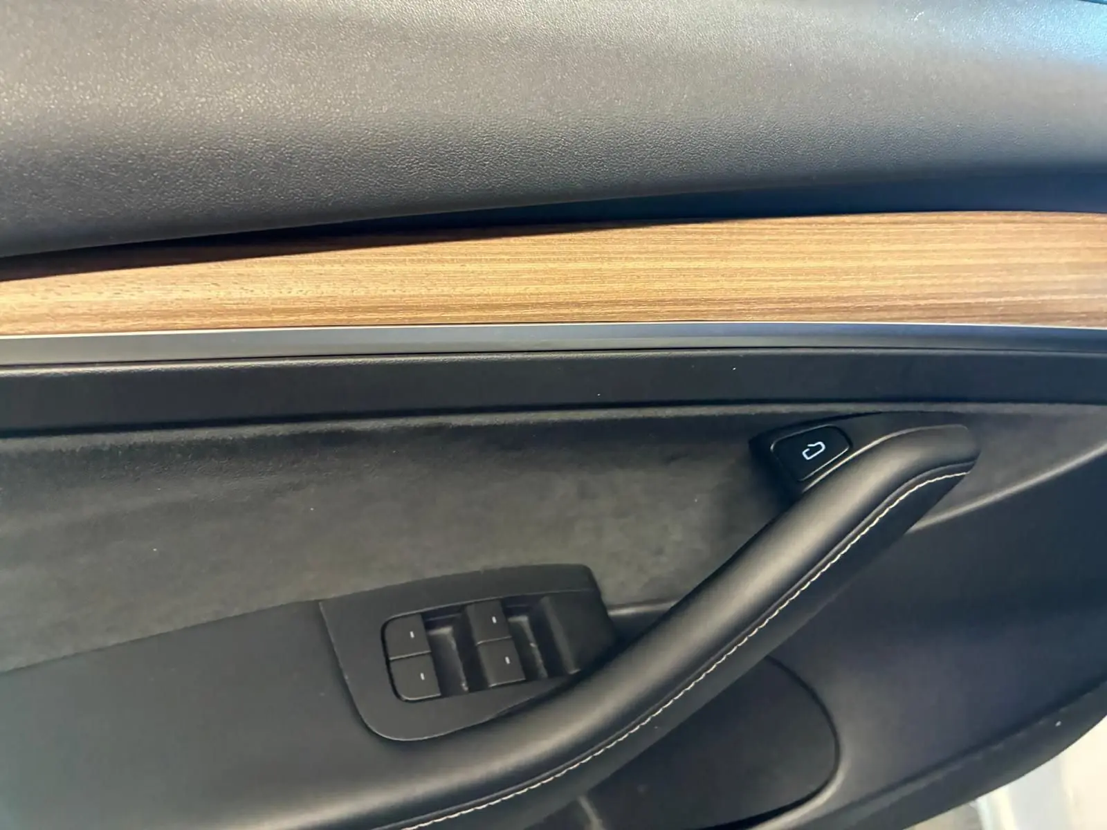Détail de la porte intérieure côté conducteur d'une Tesla Model 3 blanche 2023, avec insert bois et commandes de vitres.