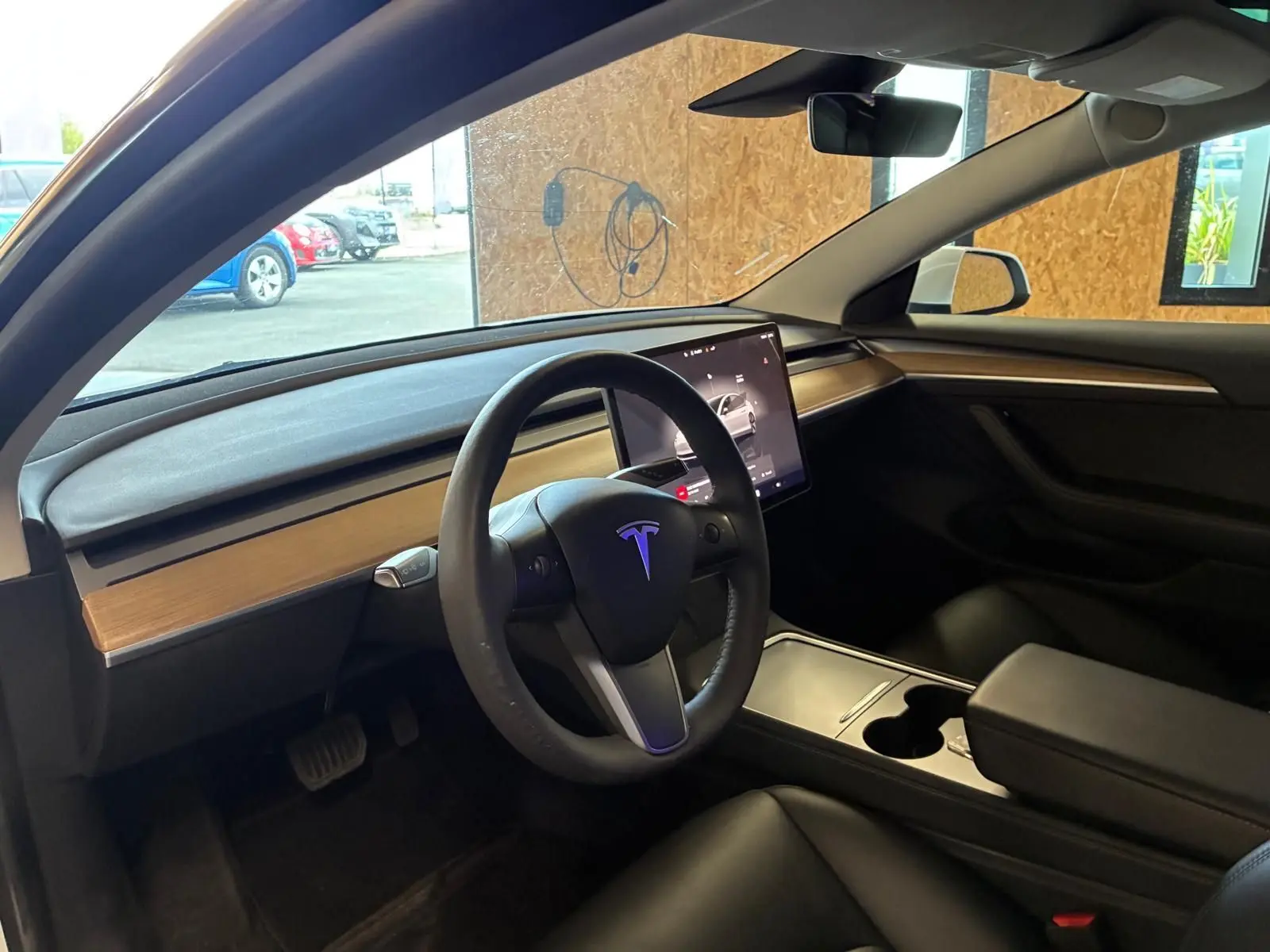 Vue intérieure côté conducteur du Tesla Model 3 blanc 2023, avec tableau de bord en bois clair et écran tactile central.