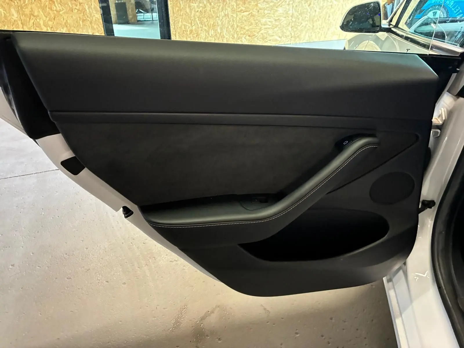 Vue intérieure de la porte avant gauche noire de la Tesla Model 3 blanche RWD 2023, avec poignée intégrée et finition épurée.