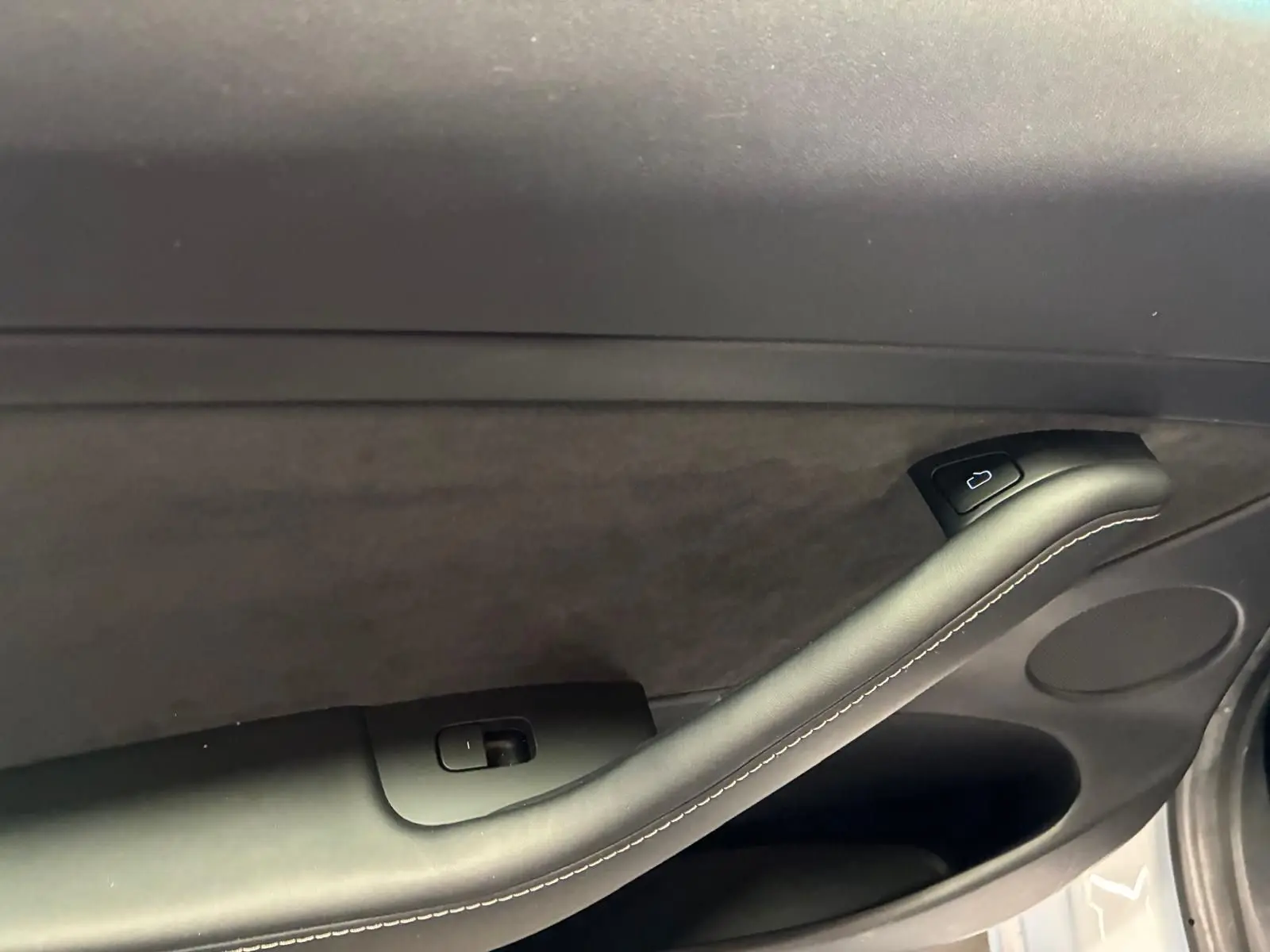 Détail de la poignée intérieure côté gauche de la porte d'une Tesla Model 3 blanche, avec bouton de verrouillage.
