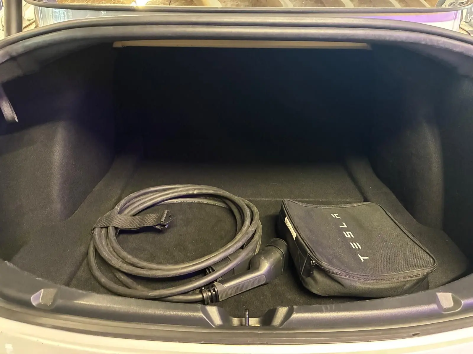 Coffre ouvert d'une Tesla Model 3 blanche 2023, vue de face, avec câble de recharge et sac de rangement Tesla.