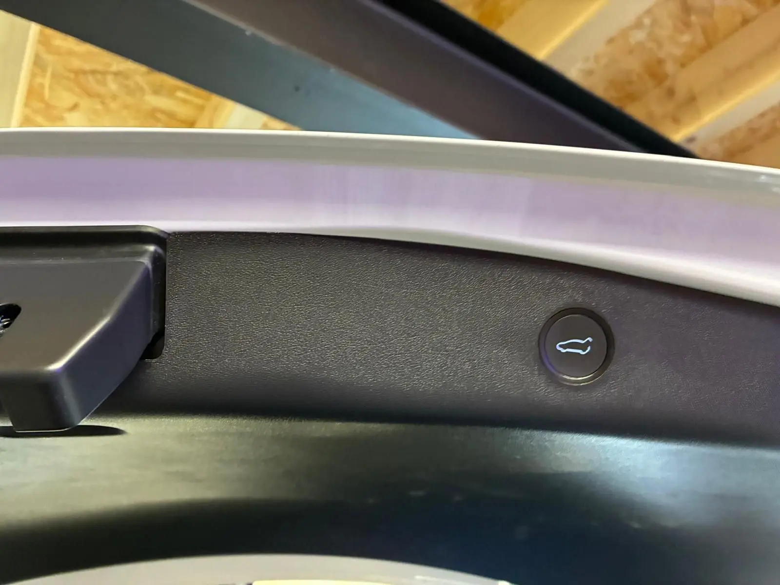 Gros plan sur le bouton d'ouverture du coffre arrière sur la partie intérieure d'une Tesla Model 3 blanche.