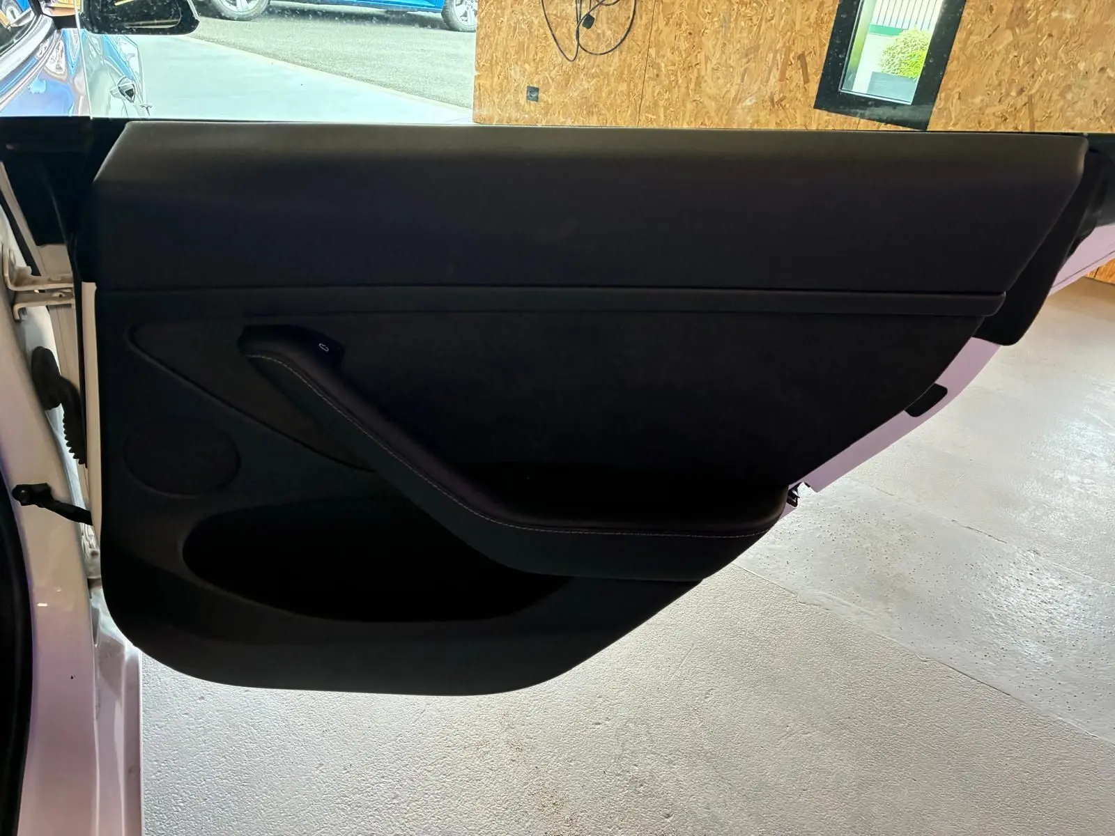 Vue intérieure de la porte côté gauche d’une Tesla Model 3 blanche, avec garniture noire minimaliste.