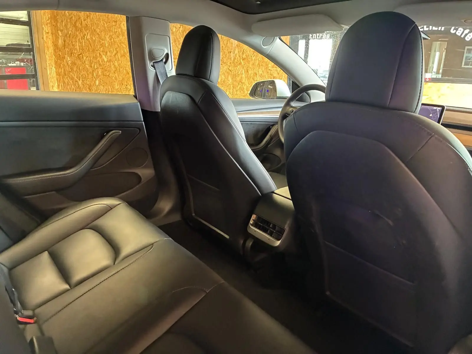 Vue intérieure arrière du Tesla Model 3 blanc 2023, montrant les sièges noirs en cuir et la console centrale avec aérateurs.