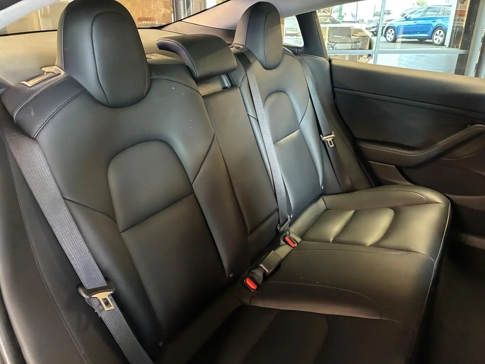 Vue intérieure des sièges arrière en cuir noir du Tesla Model 3 blanc, avec ceintures de sécurité visibles.