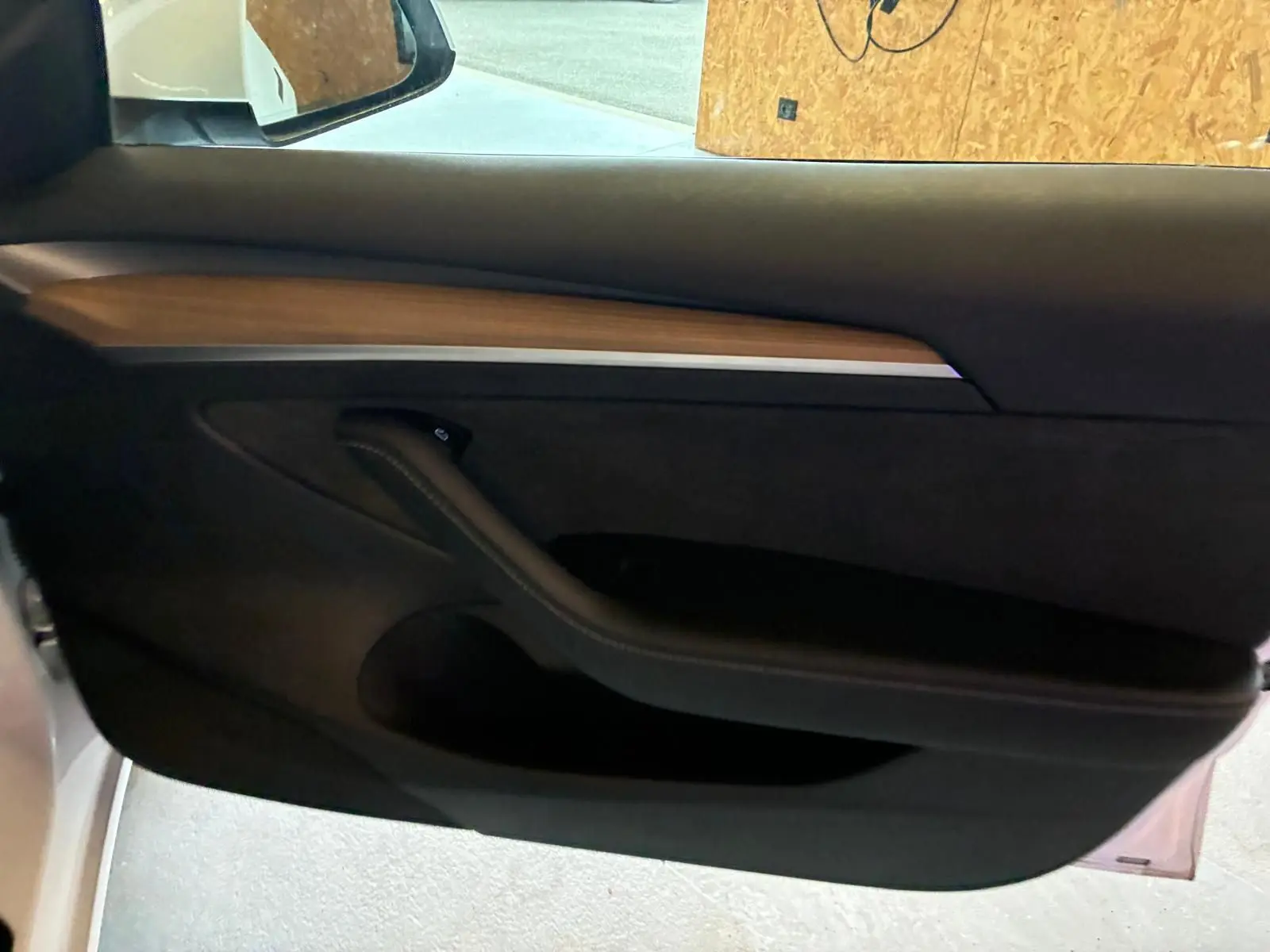 Intérieur de la porte côté conducteur d'une Tesla Model 3 blanche, avec insert en bois et poignée noire.